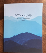 A photo of the ACTivate Vitality Personal Development planner with a soft cover and silhouette mountains in different shades of blue.